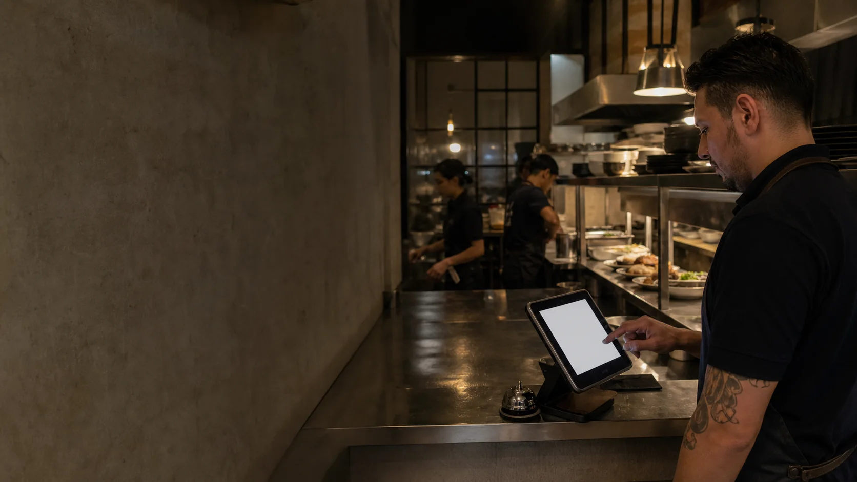 Cocinero registrando un pedido en una tableta junto a la cocina abierta